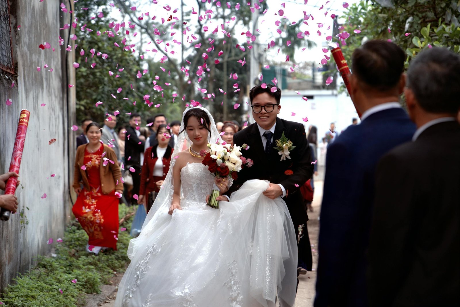 Asian couple celebrates their wedding with family amidst a petal shower, embracing love and tradition.