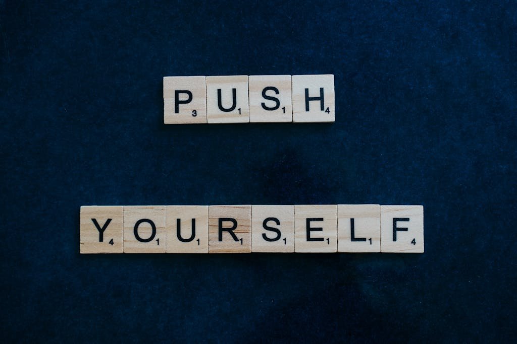 Scrabble tiles spelling 'Push Yourself' on a dark blue background, inspiring motivation.